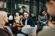 © Maskot - Smiling businesswoman discussing with colleagues while sitting on armchair during seminar in congress center