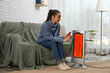 © New Africa - Woman warming her hands near electric heater at home