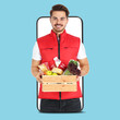 © New Africa - Delivery service worker giving order out of mobile phone against light blue background. Man with crate full of food products