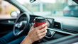 © Rafay - Hand Holding Red Coffee Cup Inside Car with Blurred Dashboard and Steering Wheel Background