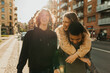 © Maskot - Portrait of smiling young man walking with male friend piggybacking female at street on sunny day