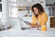 © Dorde - Professional Woman In Casual Yellow Striped Shirt Using Digital Devices While Working Remotely In Modern Bright Kitchen