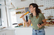 © Dorde - Young Woman Singing and Dancing in a Bright Kitchen Holding Pasta and Wearing Green Top and Jeans