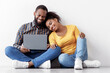 © Prostock-studio - Cheerful young black man and woman look in laptop, planning interior, sits on floor in empty room on white wall background. Relocation, buy furniture for house or working on design together, panorama