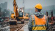 © Babb - A construction worker stands in the rain, wearing a hard hat and reflective vest, observing heavy machinery operating on a construction site surrounded by tall buildings