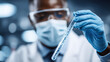 © Александр Марченко - Scientist wearing mask and goggles examining test tube with blue liquid