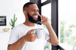 © Prostock-studio - Pleasant Conversation. Portrait of smiling African American man talking on mobile phone in the morning standing near window holding cup of hot coffee, making call with friends or family
