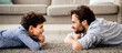 © Prostock-studio - Happy male family. Profile portrait of father and his son lying on carpet, looking at each other and smiling, spending time together at home, side view, panorama