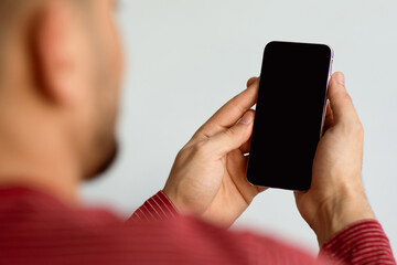 Unrecognizable arab guy using smartphone with blank screen, mockup. Cropped of middle-eastern man holding brand new mobile phone with empty display. Mobile application concept