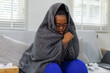 © David - African American woman wrapped on a couch,in a blanket, with flu virus blowing her nose at home.She appears to be sick or to have allergies.