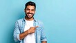 © Yudhi - Smiling, handsome man with dark hair points to the right against a bright blue backdrop. He is wearing a light denim shirt, looking confident