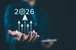 © Nirusmee - Businessman holding virtual 2026 with rising arrows and target icon, symbolizing new year business goals, future growth, strategic vision, success planning and performance improvement.