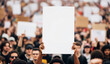 © Paylopi - A person in a large crowd of protestors holds up a blank white sign, providing a powerful mockup for a social or political message.