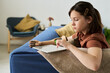 © Westend61 - Young girl with prosthetic arm using tablet on sofa at home