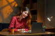 © amnaj - Asian businesswoman working late into the night at her home office, using a laptop while taking notes and staying focused on her tasks