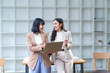 © amnaj - Two asian businesswomen discussing working using laptop and smiling each other in modern office
