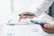 © doidam10 - Concept of financial planning and accounting. A businesswoman uses a calculator to analyze reports and charts, calculating budget and investment strategy with focus and precision at office desk.
