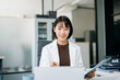 © Nuttapong punna - Asian businesswoman in blazer working on laptop at clean modern office desk.