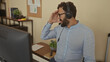 © Krakenimages.com - Hispanic man with beard wearing headset in office setting, engaging through computer for virtual communication, emphasizing modern workspace atmosphere.