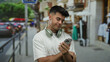 © Krakenimages.com - Young man with headphones checking smartphone on bustling city street during daytime.