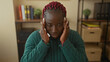 © Krakenimages.com - Woman with braids feeling stressed in an office setting with books and plants in the background, emphasizing her emotion and indoor work environment.
