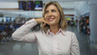 © Krakenimages.com - Blonde woman smiling with hand call gesture at brightly lit busy airport check in terminal; anticipation.