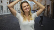 © Krakenimages.com - Young blonde woman smiling with hands above her head on a city street on a sunny day showcasing cheerful outdoor urban lifestyle.