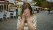© Krakenimages.com - Young caucasian woman holds hand to temples pressing fingers for headache at outdoor restaurant terrace; pain.