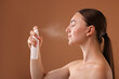 © New Africa - Beautiful woman spraying thermal water onto face on light brown background