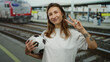 © Krakenimages.com - Woman smiling at train station holding a soccer ball showcasing peace sign with a tattoo visible against a backdrop of rail tracks and a passing train.
