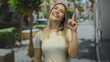 © Krakenimages.com - Woman pointing upward while smiling on a sunny city street, showcasing a cheerful urban ambiance with green trees lining the pavements.