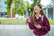 © maeching - Asian female student in warm clothes using phone to chat with friends and ready for video call while in university.