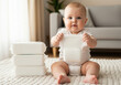 © murni - Adorable chubby baby sitting on a soft carpet in the living room, holding a clean disposable diaper with a large stack nearby