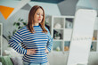 © deagreez - Young woman in striped shirt posing confidently in modern living room interior with stylish decor and bright lighting