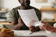 © pressmaster - Black man holding overdue bill with past due stamp while discussing financial documents with senior Caucasian woman at table, focusing on paperwork and payments