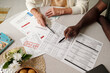 © pressmaster - Senior Caucasian woman and Black man reviewing overdue bills and financial documents at table, both pointing at paperwork with pens, discussing payment deadlines and eviction notice