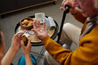 © pressmaster - Senior Caucasian man sitting with cane holding pills in hand while young adult woman assisting with medication, medical device and snacks visible on table in home setting