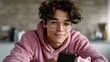 © Thares2020 - Smiling teenager with glasses uses a smartphone app managing savings and learning about finance with a piggy bank nearby