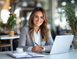 © TENphoto - Professional woman smiling while working on a laptop in a bright cafe
