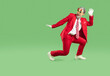 © Studio Romantic - Cheerful, extravagant, stylish, young Santa Claus dressed in stylish red suit and striped tie is fooling around and dancing. Studio full-size photo on isolated green background.