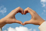 Two hands forming a heart shape against a blue sky with clouds love symbol