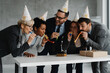 © Novak - Group of business people in office celebrating birthday with cake, party hats and blowers. Corporate celebration, teamwork and cheerful workspace atmosphere