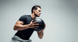 Muscular man doing a fitness workout with a medicine ball. Athlete focused on strength training and crossfit exercise on a grey background with copy space.