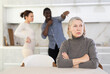 © JackF - Sad old woman sitting at the kitchen table with her back to middle-aged couple quarreling together