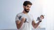 © Prostock-studio - New normal and social distancing, strength training at home, modern workout and bodybuilding. Cheerful millennial bearded arabian male lifting dumbbells in minimalist living room interior, copy space