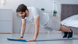 © Prostock-studio - Online workout, coach remotely and home exercises during covid-19 lockdown. Smiling attractive arabian male with beard makes plank and looks at laptop on floor in bedroom interior in morning