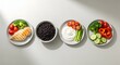 © XBRP.studio - Four small plates of healthy food, featuring grilled chicken, black beans, vegetables, and a creamy sauce, arranged in a row on a light background.