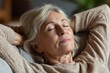 © LimeSky - Side view of a serene elderly woman with eyes shut resting her hands behind her head as she drifts off in a snug living room experiencing a peaceful stress free retirement