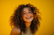 © EricMiguel - Joyful young woman with curly hair laughing against vibrant yellow background in natural light