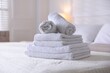 © New Africa - Stack of clean towels on bed linens at home, closeup